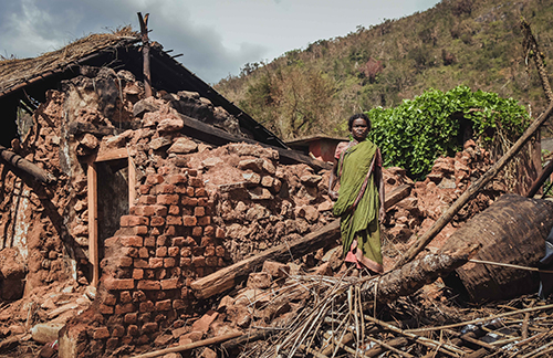 Image of an older woman standing on her collapsed house